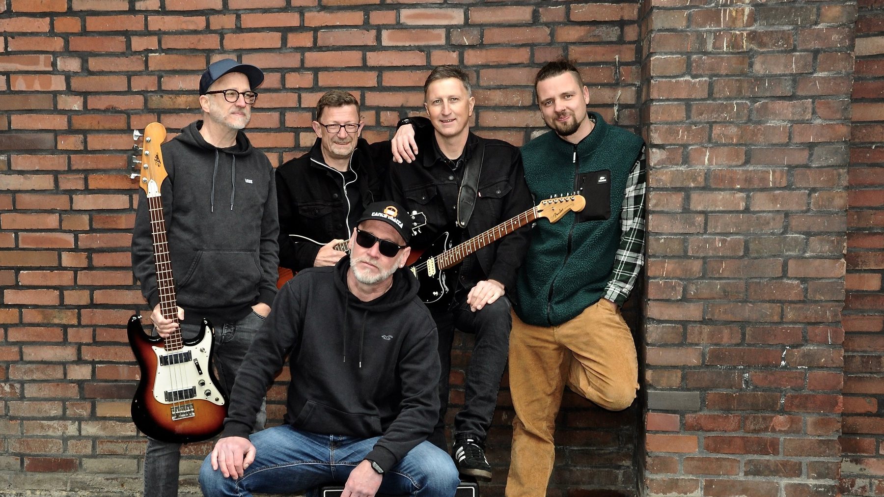 Die fünf von Tante Matta vor einer Backsteinmauer, mit Bass und Gitarre